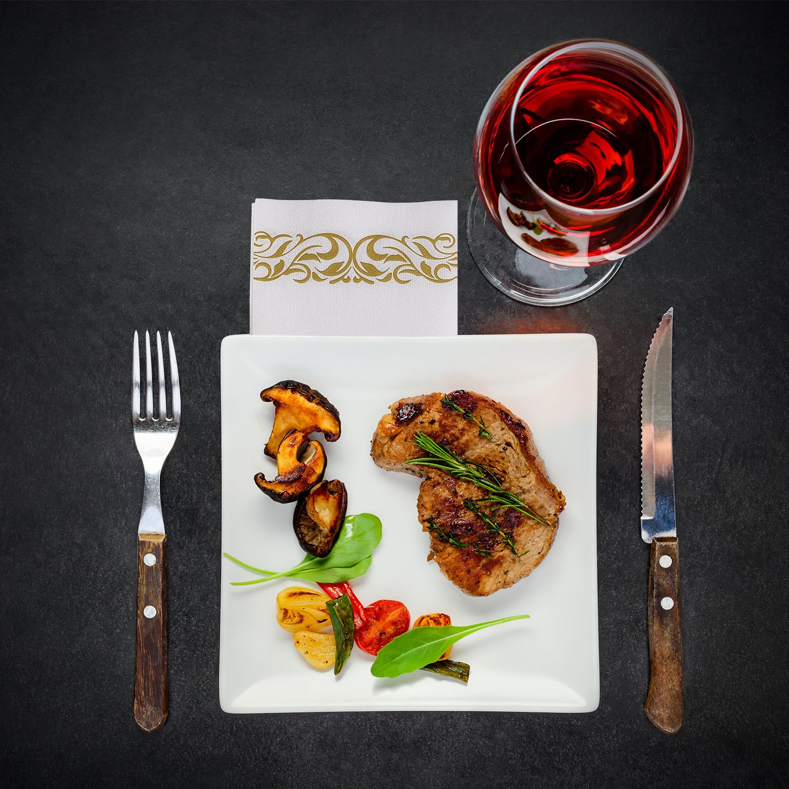 Plated dish with meat and vegetables, accompanied by a glass of red wine, fork, and knife on a dark surface.