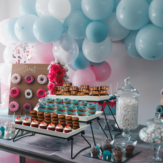 Decorative dessert table with balloons, donuts, and cupcakes against a light pink wall.
